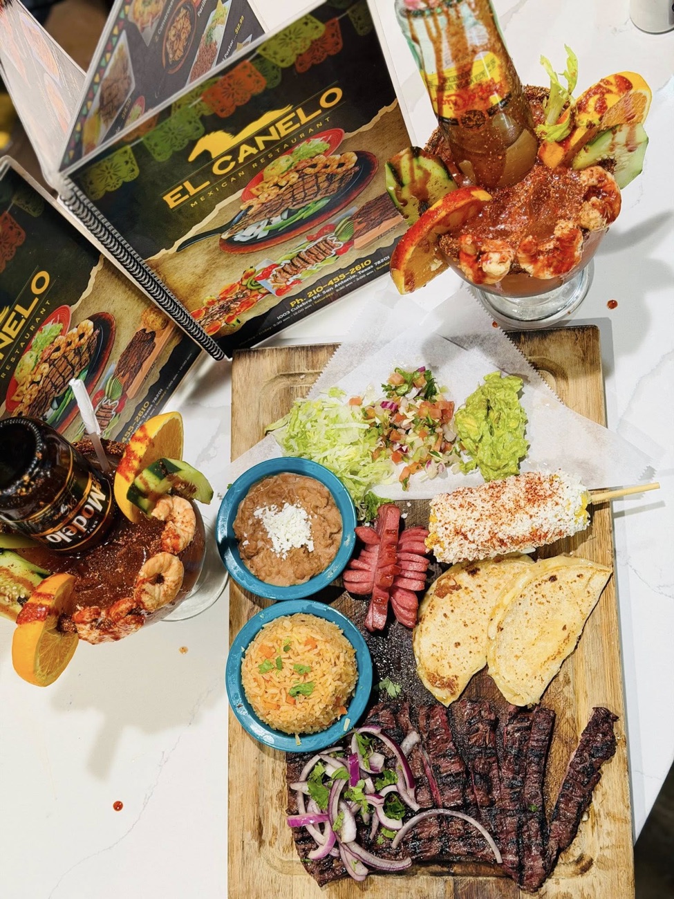 Parrillada overhead shot — arrachera, sausage, guacamole, and a michelada
