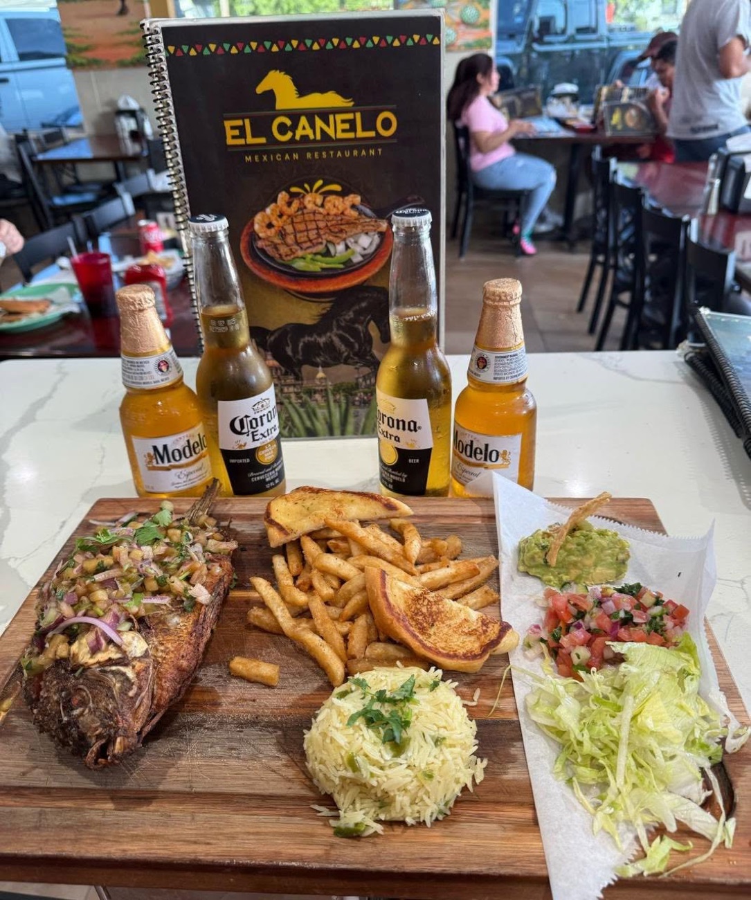 Whole fish on a board with fries, pico de gallo, and Corona beers