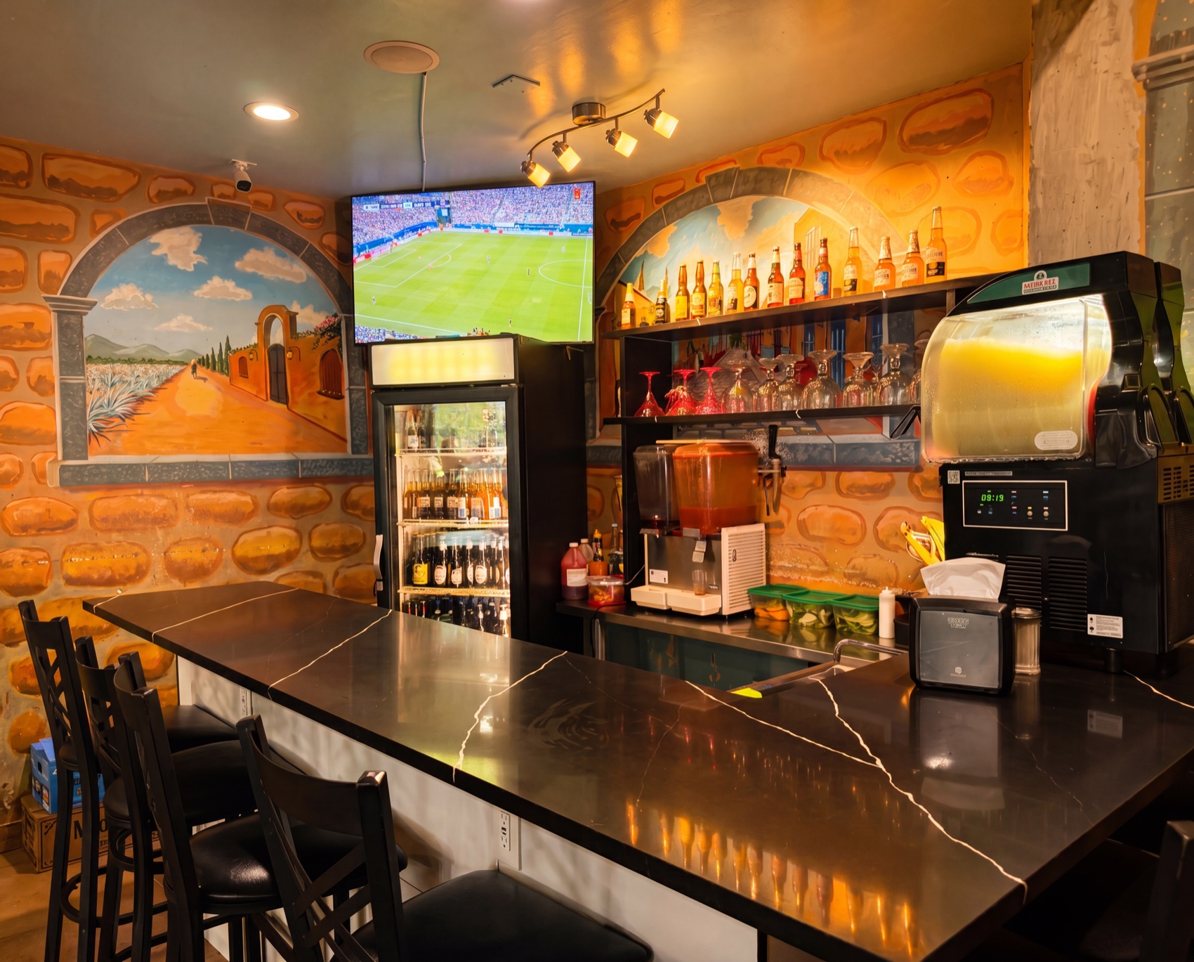 El Canelo cantina bar — marble counter, margarita machines, and mural